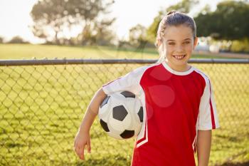 Schoolgirl in football strip holding ball, smiling to camera