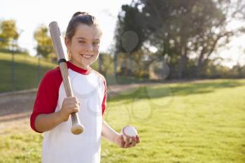 Young girl holding baseball and baseball bat looks to camera