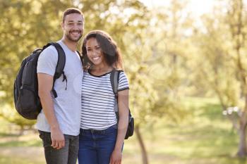 Portrait Of Couple Wearing Backpacks Hiking In Park Together