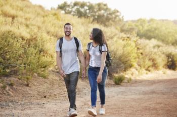 Couple Wearing Backpacks Hiking In Countryside Together