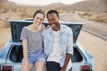 Portrait Of Couple Sitting In Trunk Of Classic Car On Road Trip