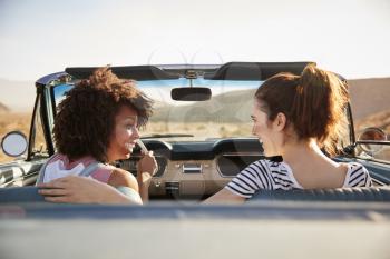 Two Female Friends Enjoying Road Trip In Open Top Classic Car