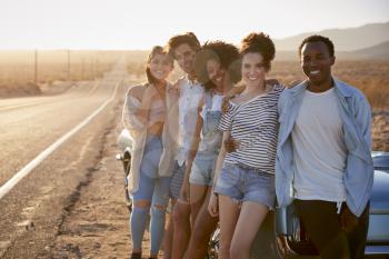 Portrait Of Five Friends Standing By Convertible Classic Car On Road Trip