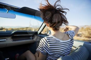 Rear View Of Female Passenger On Road Trip In Classic Convertible Car