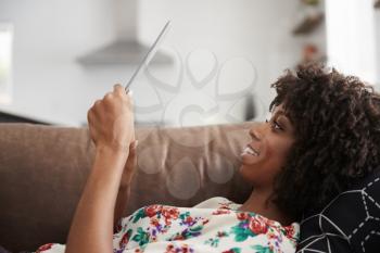 Woman Lying On Sofa At Home Using Digital Tablet