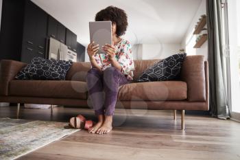 Woman Sitting On Sofa At Home Using Digital Tablet