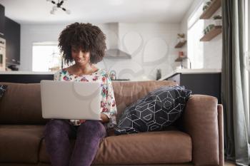 Woman Sitting On Sofa At Home Using Laptop