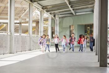 Primary school kids run holding hands in school corridor