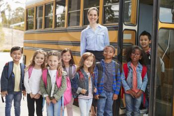 Elementary school teacher and pupils standing by school bus