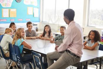 Male teacher with elementary school kids in class discussion
