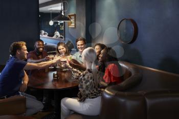 Group Of Young Friends Sitting Around Table And Making A Toast In Bar On Night Out