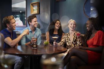 Group Of Young Friends Sitting Around Table In Bar Together On Night Out