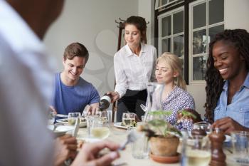 Waitress Pouring Wine For Group Of Friends Enjoying Meal In Restaurant Together