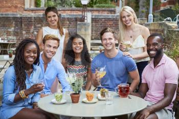 Portrait Of Friends Sitting At Table In Pub Garden Enjoying Drink Together