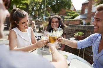 Friends Sitting At Table In Pub Garden Making Toast Together