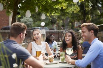 Friends Sitting At Table In Pub Garden Enjoying Drinks Together
