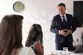 Mature Businessman Addressing Group Meeting Around Table At Graduate Recruitment Assessment Day