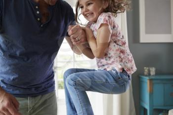 Girl jumping up and holding dads hand at home, mid section