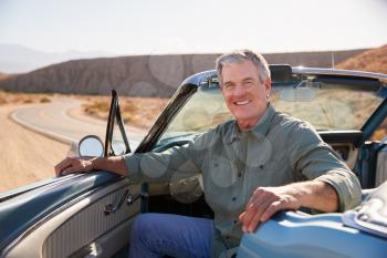 Senior man smiling to camera from parked open top car