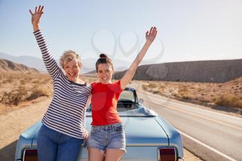Mum and adult daughter on road trip stand waving to camera