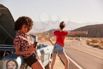 Two female friends by their broken down car at the roadside