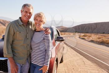 Senior white couple standing on desert roadside by car