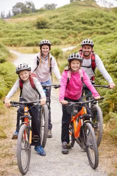 Parents and children sitting on mountain bikes in a country lane during a family camping trip, full length
