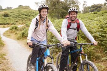 Young adult couple sitting on mountain bikes in a country lane during a camping holiday, close up