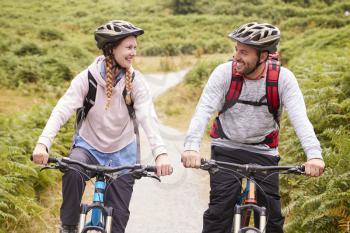 Young adult couple riding mountain bikes in a country lane, looking each other, close up