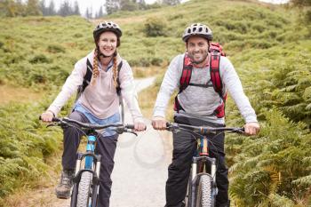 Young adult couple riding mountain bikes in a country lane, looking at camera, close up