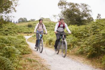 Young adult couple riding mountain bikes in the countryside, full length