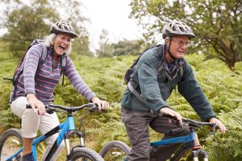 Senior couple riding mountain bikes in the countryside during a camping holiday, side view, close up