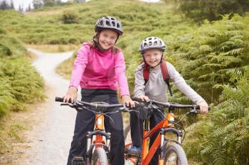 Two children sitting on their mountain bikes on a country path laughing, front view