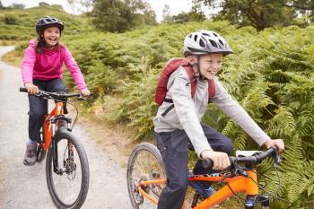 Two children riding mountain bikes on a country path laughing, selective focus