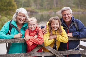 Grandparents and grandchildren leaning on a wooden fence in the countryside laughing, Lake District, UK