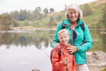 Grandmother and grandson standing together near a lake in the countryside smiling to camera, close up, Lake District, UK