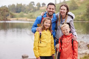 Young family standing on the shore of a lake in the countryside looking to camera smiling, Lake District, UK