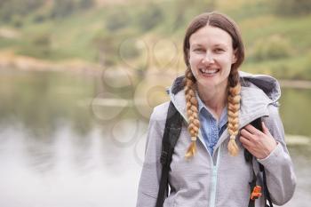 Young adult woman on a camping holiday standing by a lake laughing, portrait, Lake District, UK