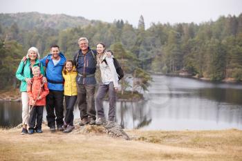 Multi generation family stand embracing by a lake, smiling to camera, front view, Lake District, UK