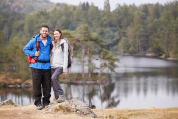 Young adult couple standing on a rock beside a lake in countryside, smiling to camera, full length