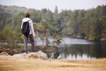 Young adult woman standing on a rock admiring the view of a lake, back view, Lake District, UK