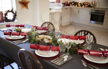 Christmas table setting with Christmas crackers arranged on plates in a dining room, with kitchen in the background