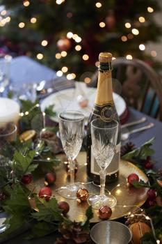 Christmas table setting with glasses and a bottle of champagne, baubles arranged on a gold plate and green and red table decorations, vertical