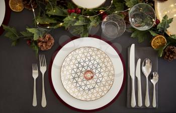 Christmas table place setting with bauble arranged on a plate and green and red table decorations, overhead view