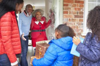 Grandparents Greeting Mother And Children As They Arrive For Visit On Christmas Day With Gifts