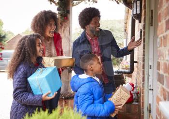 Family Standing At Front Door As They Arrive For Visit On Christmas Day With Gifts