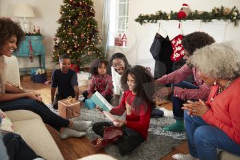 Daughter Opening Gift As Multi Generation Family Celebrate Christmas At Home Together
