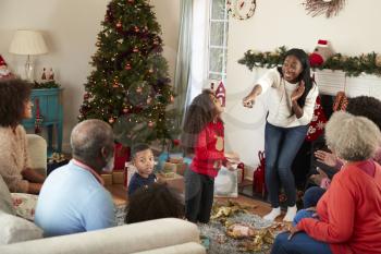 Multi Generation Family Playing Game Of Charades As They Celebrate Christmas At Home Together