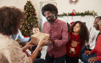 Couple Exchanging Gifts As Multi Generation Family Celebrate Christmas At Home Together