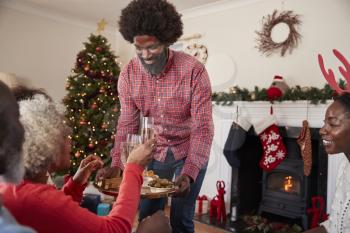 Man Serving Champagne And Snacks As Adult Members Of Family Celebrate Christmas At Home